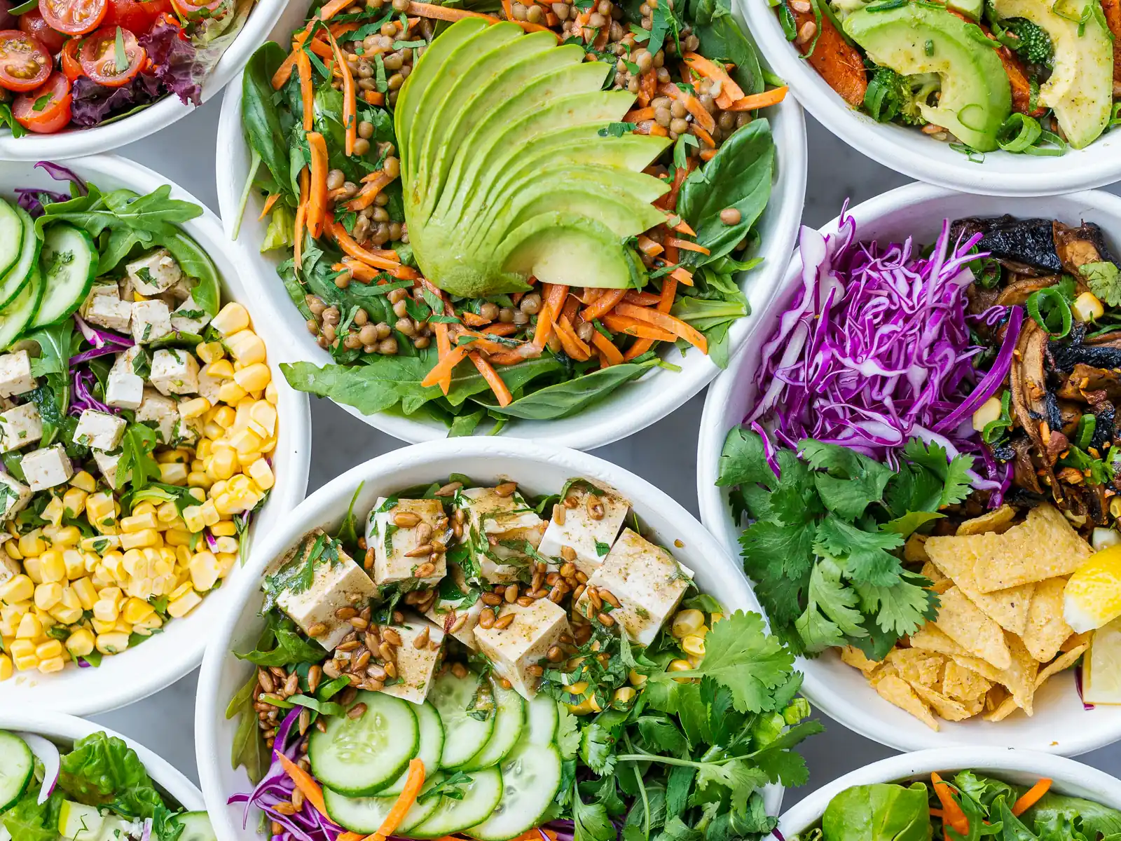A table spread with colourful bowls of grains, greens and vegetables, seen from above in daylight